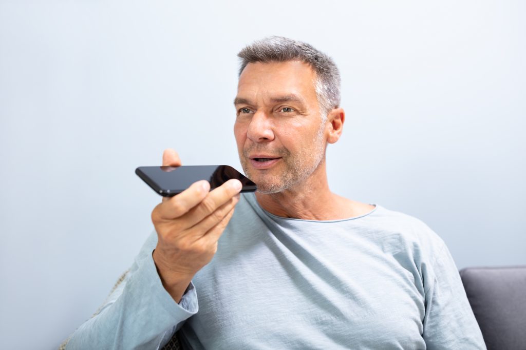 Close-up Of A Beard Man Using Voice Recognition Function On Mobile Phone Against White Background